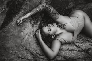 Black-and-white portrait of a woman reclining against a natural rock formation with her eyes closed.